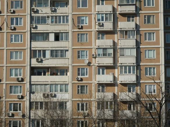 Front view of a sunlit urban apartment building with balconies and air conditioning units.