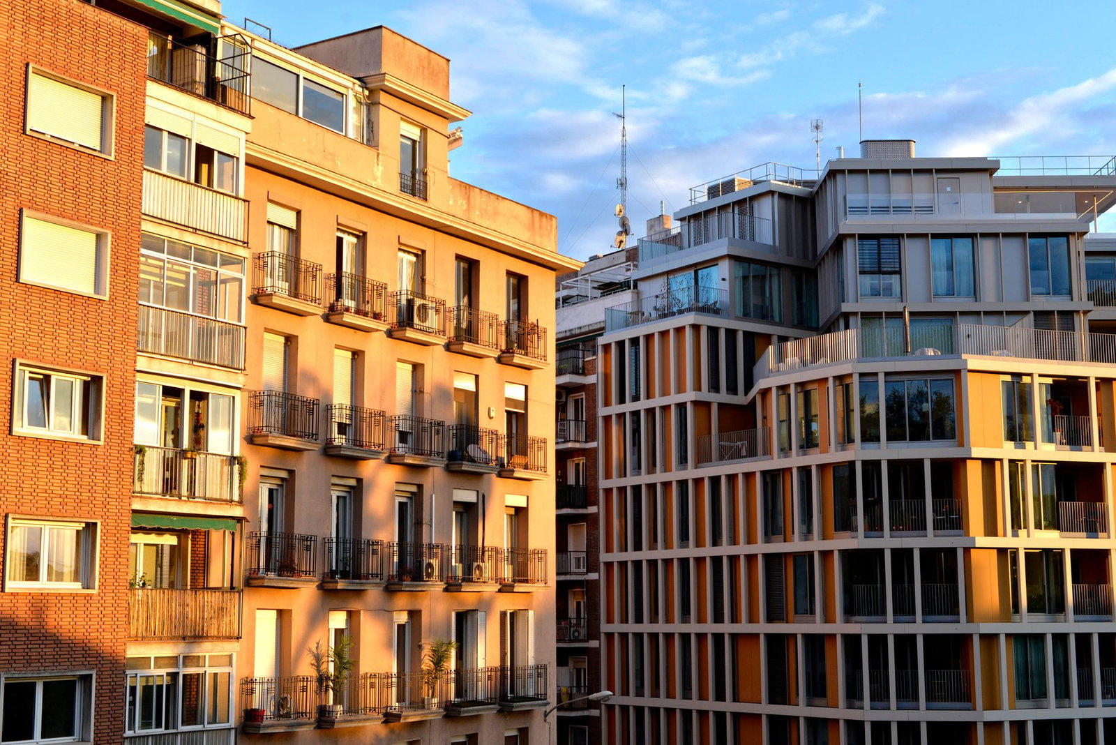 Sunlit modern and classic residential facades with balconies and glass windows against a blue sky.