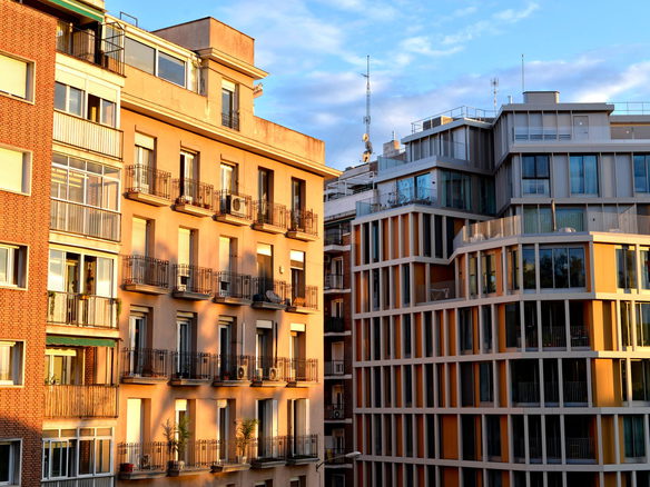 Sunlit modern and classic residential facades with balconies and glass windows against a blue sky.